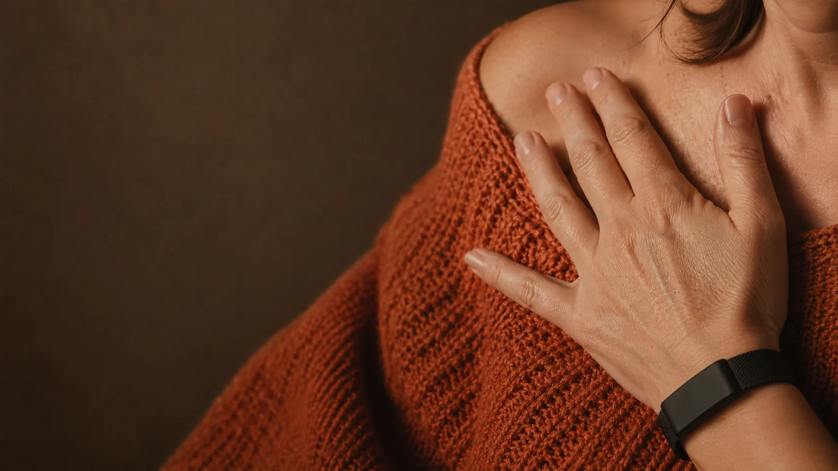 Person in a rust-colored knit sweater with a hand resting near their shoulder, wearing a black sleep tracker band