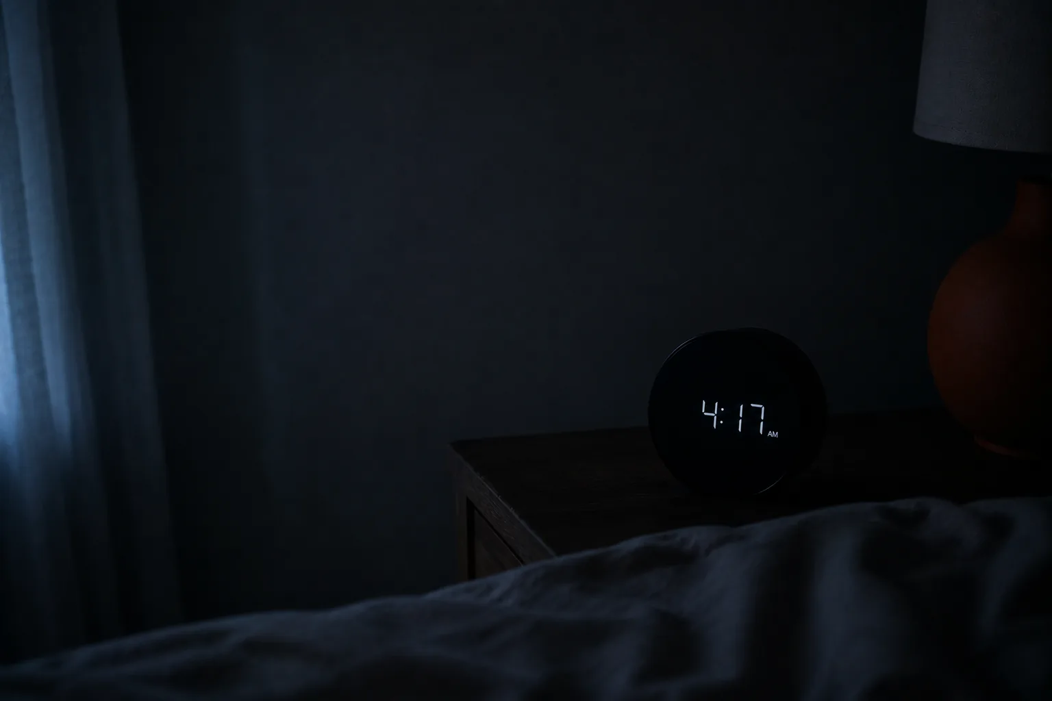 A quiet bedroom window before dawn with soft grey light coming in, a made bed and a still, calm room